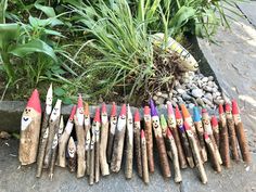 several wooden sticks with faces painted on them are lined up next to some rocks and plants