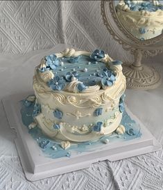 a white and blue cake sitting on top of a table next to a small mirror