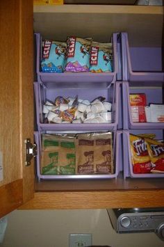 an organized pantry drawer filled with snacks and other items in purple bins on top of a wooden cabinet