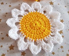 a crocheted flower with yellow center sitting on a white tablecloth next to a pair of scissors