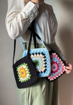 a woman holding three crocheted purses on her shoulder and looking at the camera