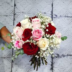 a woman holding a bouquet of roses in front of a tile wall with white and red flowers