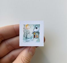 a hand holding a small card with a house on it and trees in the background