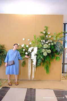 a woman standing in front of a flower display with white flowers and greenery on the wall