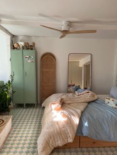 a bed room with a neatly made bed next to a green cabinet and mirror on the wall