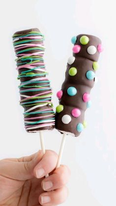 a hand holding two chocolate covered lollipops with sprinkles on them