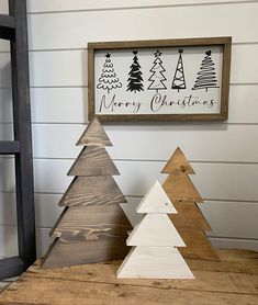 three wooden christmas trees sitting on top of a table next to a sign that says merry christmas