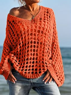 a woman standing on the beach wearing an orange crochet sweater with sleeves down