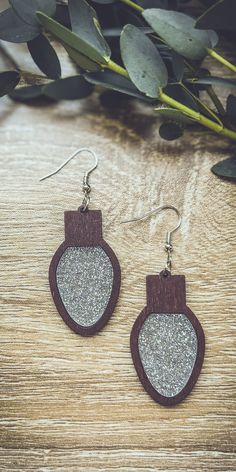 two wooden earrings with silver glitter on them sitting on top of a wooden table next to eucalyptus leaves