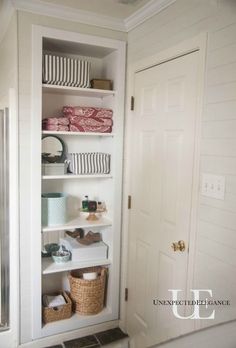 an open bathroom closet with shelves and baskets on the bottom, in front of a white door