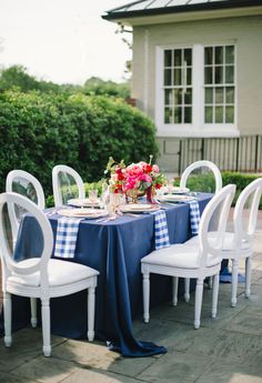 the table is set with blue and white linens, flowers, and plates on it