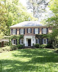 a large brick house with black shutters and white trim on the windows, surrounded by lush green grass