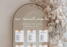 wedding seating chart displayed in front of mirror with white flowers and dried branches behind it