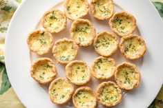 small appetizers are arranged on a white plate with green flowers in the background