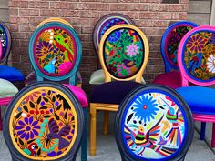 several colorful chairs with designs on them are lined up in front of a brick wall