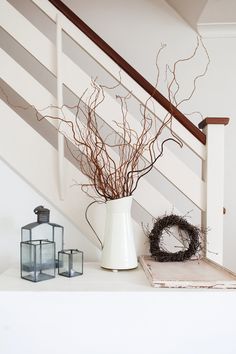 a white vase filled with branches on top of a shelf next to a candle holder