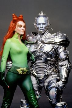 two people dressed in green and silver standing next to each other, one wearing a robot suit