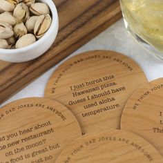 four wooden coasters with words on them next to a bowl of nuts and a drink