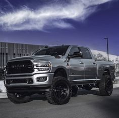 a gray ram truck parked in front of a building with large tires on it's tires