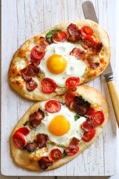 two pizzas with eggs and bacon on them sitting on a cutting board next to a fork