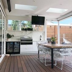 an outdoor kitchen and dining area with wood flooring, white walls and wooden floors