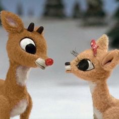 two stuffed deers are standing in the snow with one looking at the other's nose