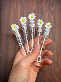 five plastic daisies are in the palm of a person's hand on a wooden table