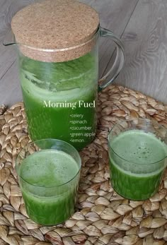 two glasses filled with green liquid sitting on top of a woven place mat next to a jug