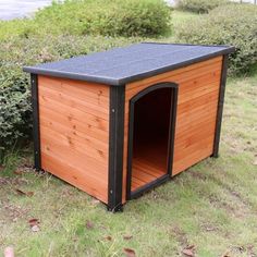 a wooden dog house in the middle of a grassy area with trees and bushes behind it