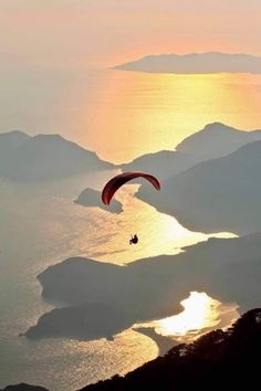 a paraglider is flying over the ocean at sunset with mountains in the background