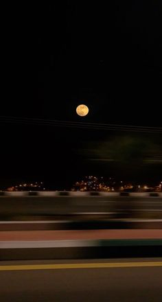 a full moon is seen in the night sky over a city street with cars passing by