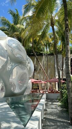 a large white object sitting on top of a pool next to palm trees and umbrellas