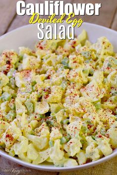 a white bowl filled with cauliflower salad on top of a wooden table next to a