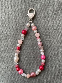 a pink and white beaded bracelet on a gray surface with a silver charm hanging from it's end