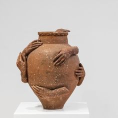 a large clay vase with two hands on it's face and arms wrapped around the body