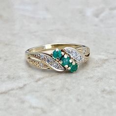 Vintage 14 karat yellow gold cocktail ring set with 3 natural round emeralds weighing approximately 0.20 carat. It is surrounded by approximately 0.05 carat of near colorless single cut diamonds that are slightly included (SI clarity). Size 4 US. (Can be sized). Weighs 2 grams. Birthstone: April/May. Condition: Very good. Light scratches throughout metal. - 14 day return policy, no questions asked. - Free insured shipping in the US. - International shipping available. Note: This item has been ap Green 14k Gold Cluster Ring For Anniversary, Anniversary 14k Gold Green Cluster Ring, Emerald Multi-stone Rings For Anniversary, Cluster Ring For Anniversary With May Birthstone, Classic Multi-stone Emerald Ring For Anniversary, Emerald Multi-stone Birthstone Ring For Anniversary, Heirloom Cluster Ring For Anniversary With May Birthstone, Heirloom Style Emerald Cluster Ring For Anniversary, Heirloom Cluster Emerald Ring For Anniversary