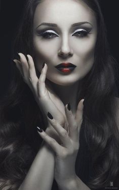 a woman with long dark hair and red lipstick posing for the camera, her hands on her face