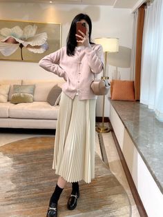 a woman taking a selfie in front of a mirror wearing a pink sweater and pleated skirt