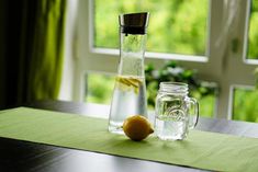 a glass pitcher with water and an orange sitting on a table next to a window