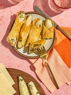 a plate with cucumbers and cheese on it next to a knife and fork