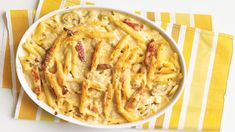 pasta with bacon and cheese in a white dish on a yellow and white striped tablecloth