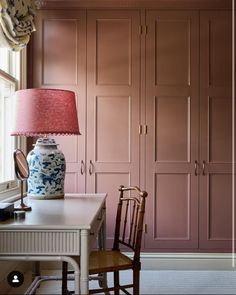 a room with pink painted walls and a white table with a lamp on it next to a chair