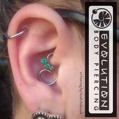 an ear piercing with two green jeweled stones in it's middle and on the side