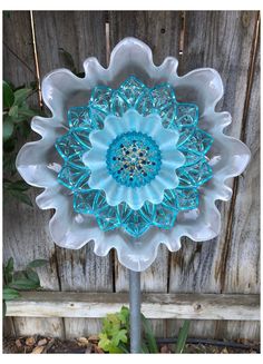 a blue and white glass flower sitting on top of a metal pole in front of a wooden fence