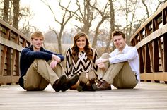 three young people sitting on a bridge posing for a photo with trees in the background