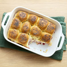 a casserole dish with rolls in it on a green towel next to a wooden table