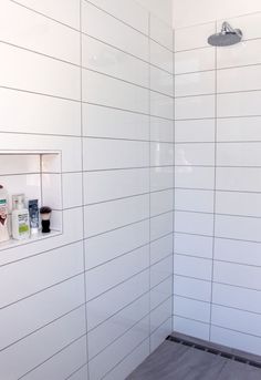 a white tiled bathroom with wood flooring and shower head mounted to the side of the wall