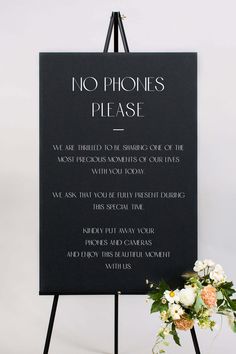 a sign that says no phones please with flowers in front of it and a vase on the side