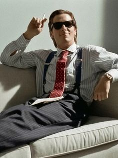 a man sitting on top of a white couch wearing sunglasses and a tie with suspenders