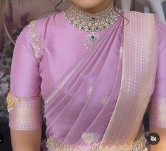 a woman in a pink sari with gold jewelry on her neck and shoulder, looking at the camera